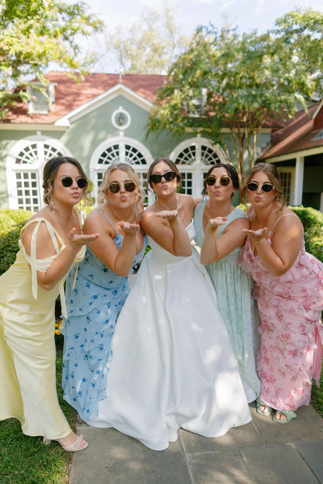 Bride and her bridesmaids in mismatched pastel dresses blowing kisses to the camera