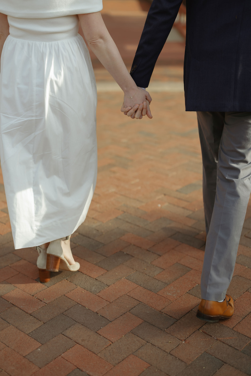 Close-up of a couple's held hands walking a brick path during their Smithsonian Castle engagement session in Washington DC