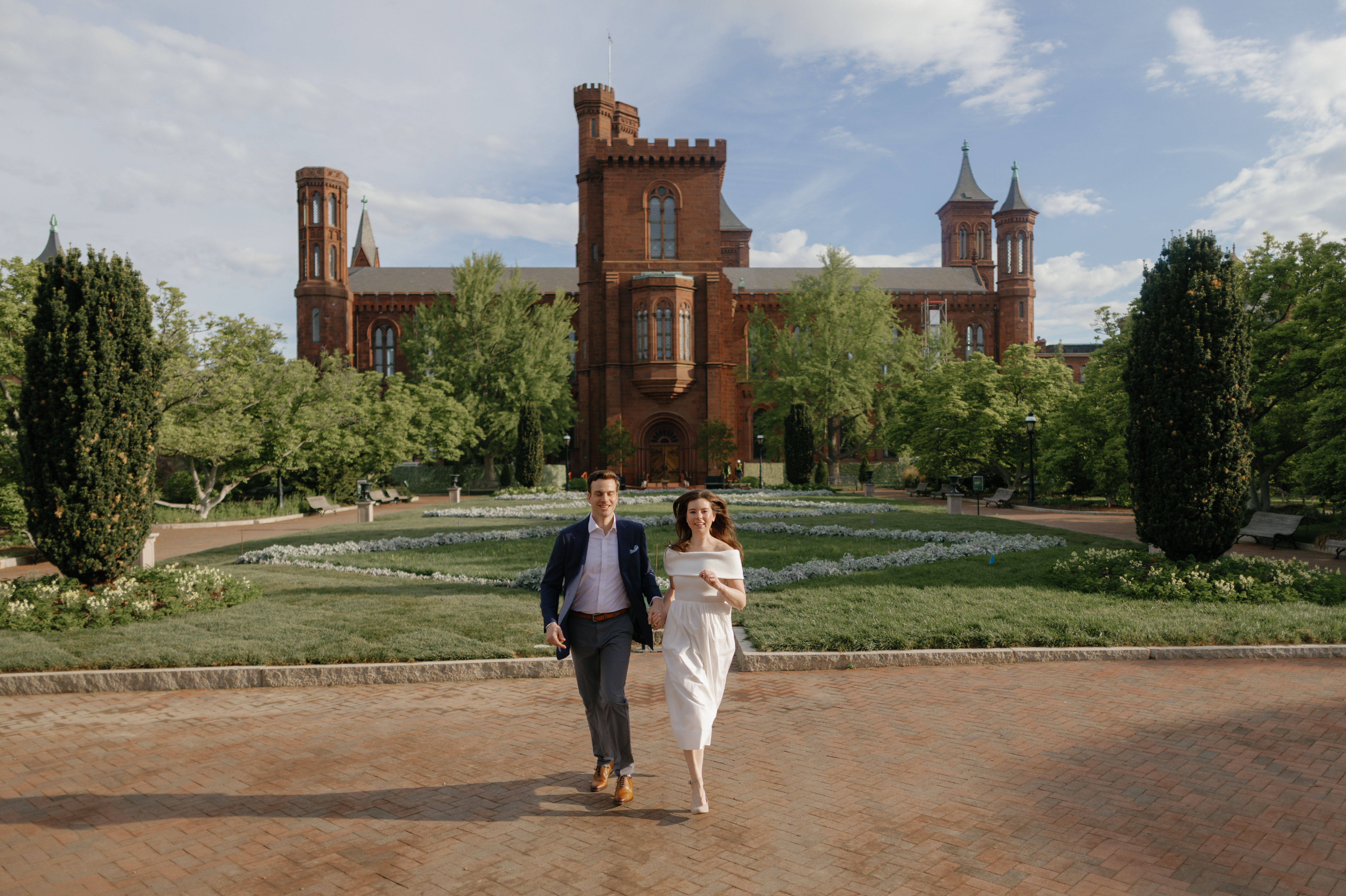 Engaged couple running through the parterre garden in front of the Smithsonian Castle at sunrise